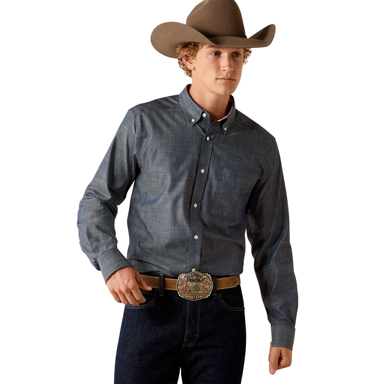 A man wearing a long-sleeve button-down western shirt in a dark blue-gray color, paired with a brown cowboy hat, dark blue jeans, and a brown leather belt with a large silver buckle, photographed against a solid white background.