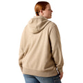 A woman with red hair tied back, viewed from the back, wearing a light beige heathered pullover hoodie and blue jeans against a plain white background.