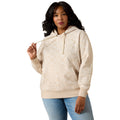 A woman modeling a cream-colored patterned hoodie with drawstrings and a front kangaroo pocket, paired with light blue jeans, against a solid white background.