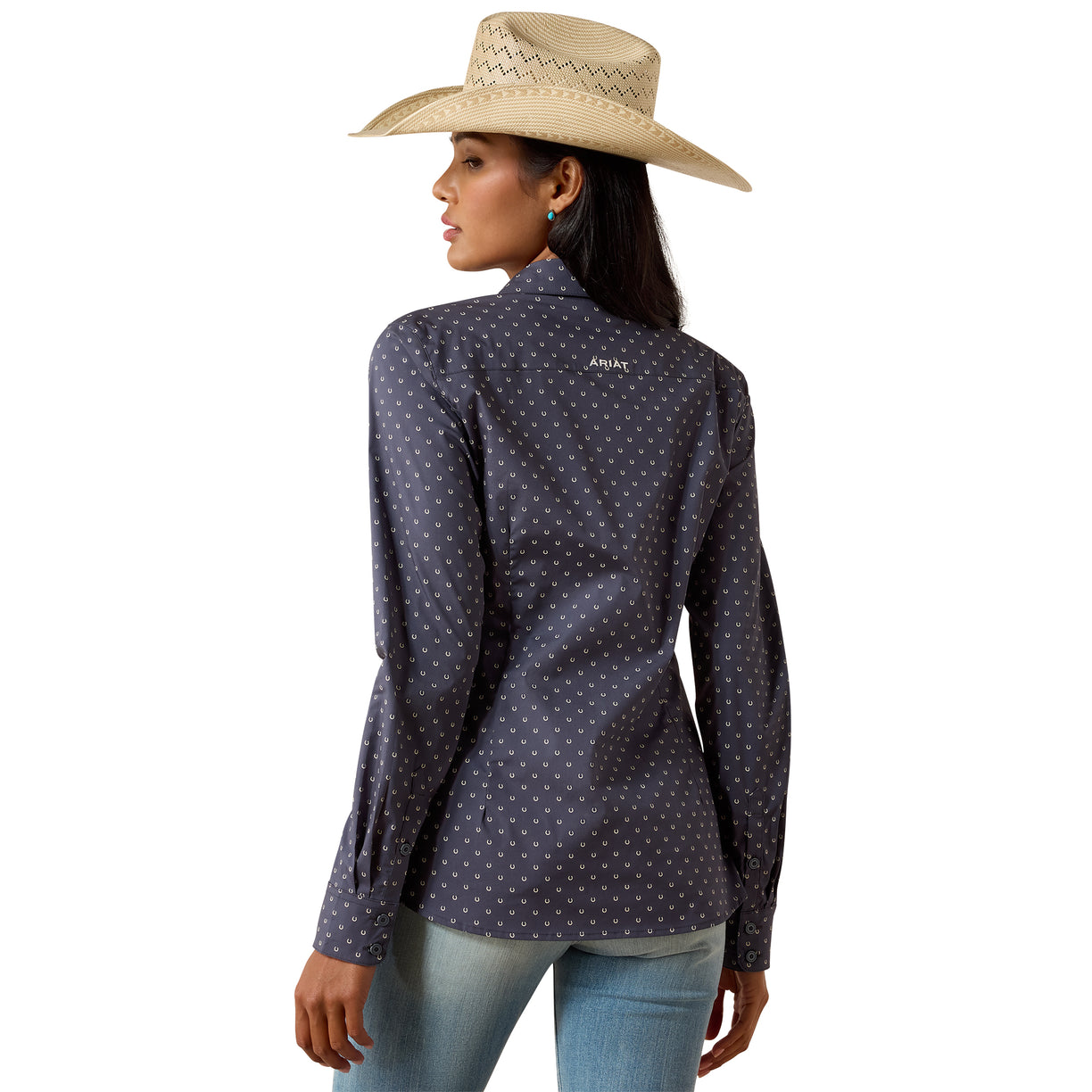 A woman wearing a dark navy long-sleeve western shirt with a small white polka dot pattern, paired with a beige straw cowboy hat and light blue jeans, shown from a rear three-quarter view against a white background.