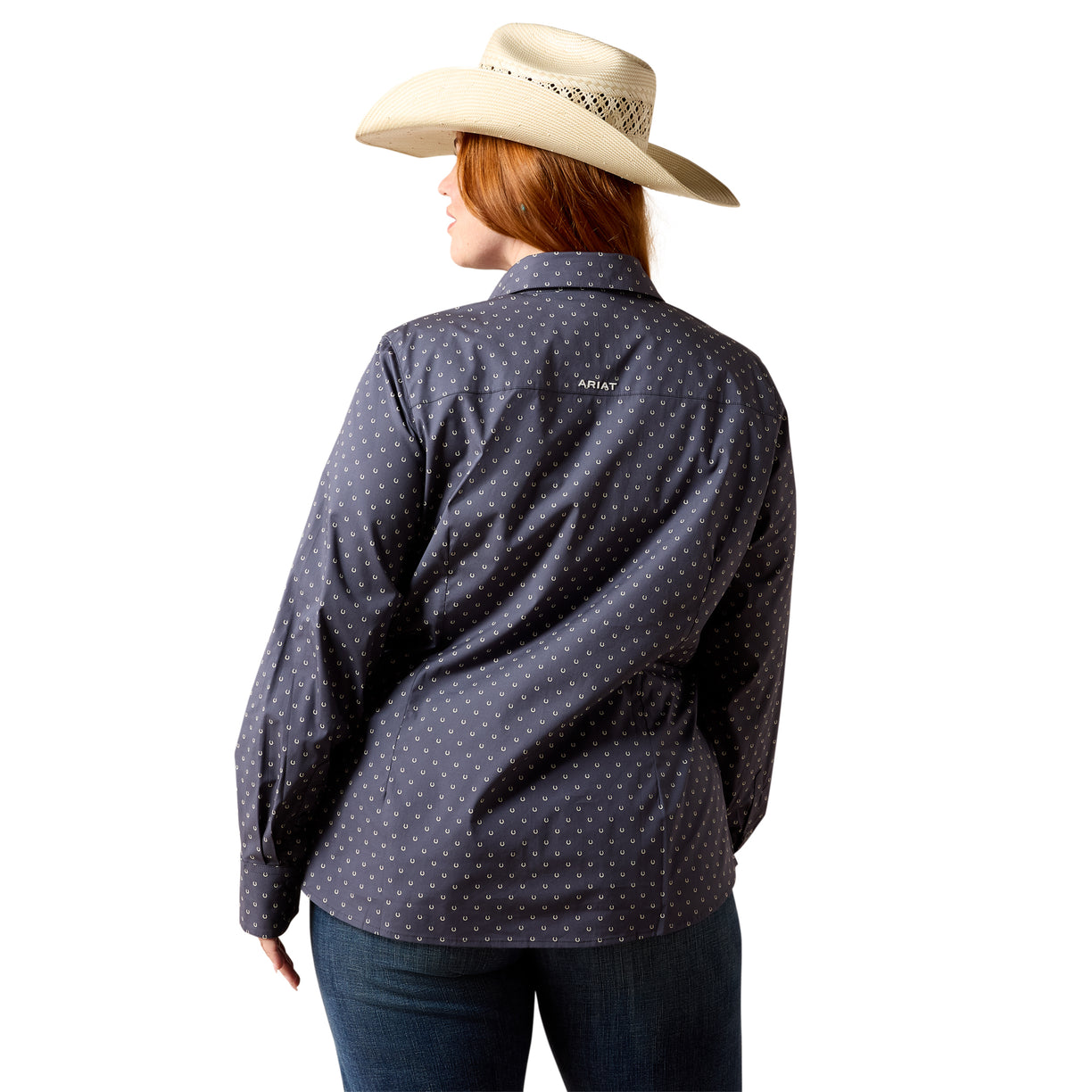 A woman shown from the back wearing a dark navy long-sleeve button-up shirt with a small white polka dot pattern, paired with a beige cowboy hat and dark jeans, against a solid white background.