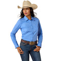 A woman modeling a light blue long-sleeve western-style button-up shirt, paired with dark blue jeans, a brown leather belt, and a beige cowboy hat, against a plain white background.