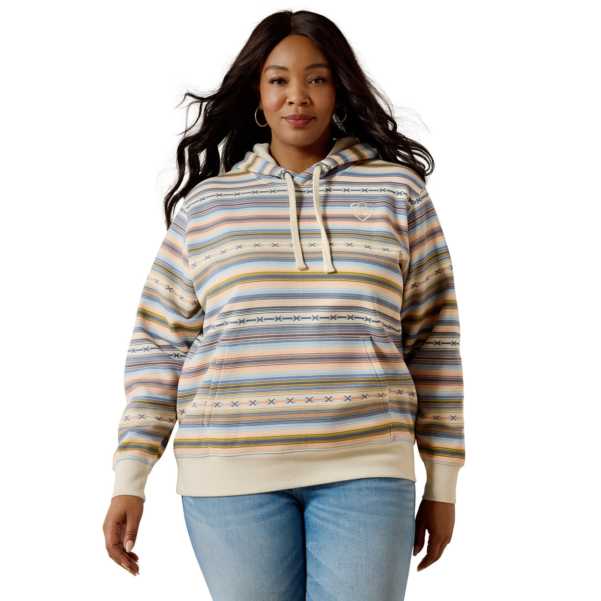 A woman modeling a striped pullover hoodie with a multicolor pattern of beige, blue, yellow, and brown horizontal stripes, paired with light blue jeans against a plain white background.