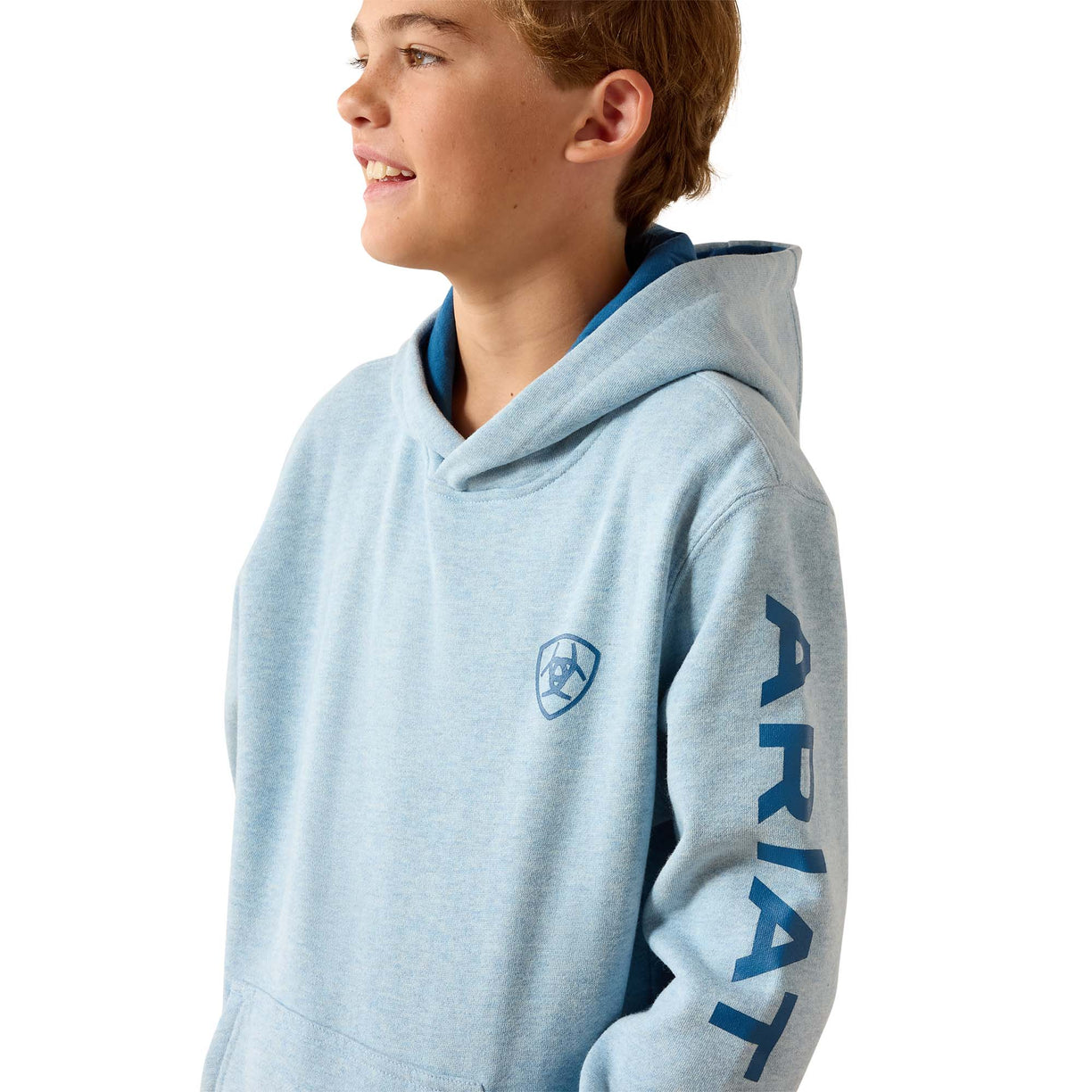 A light blue heathered hoodie with a dark blue interior hood lining and sleeve print, worn by a young male model in profile against a white background. The hoodie features a shield logo on the left chest and the brand name 'ARIAT' printed vertically on the right sleeve.