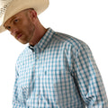 A man wearing a light blue and white gingham button-down shirt and a cream cowboy hat, shown in a close-up profile against a white background.