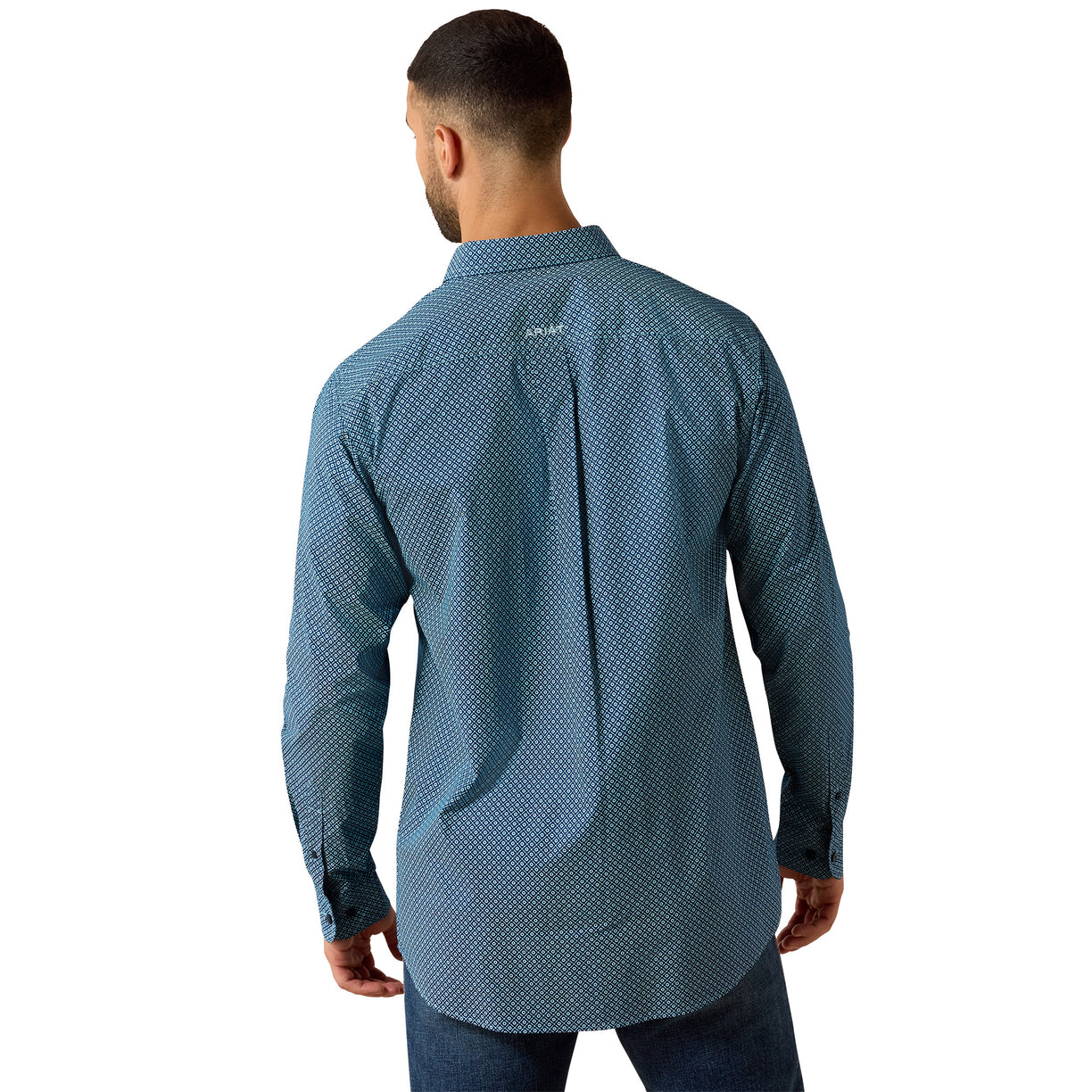 A man viewed from the back wearing a blue long-sleeve button-up shirt with a small white geometric pattern, paired with dark blue jeans against a plain white background.