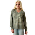 A blonde woman modeling an olive green long-sleeve V-neck sweatshirt with a distressed beige 'Desert Wild West' graphic on the front, paired with light blue jeans against a plain white background.