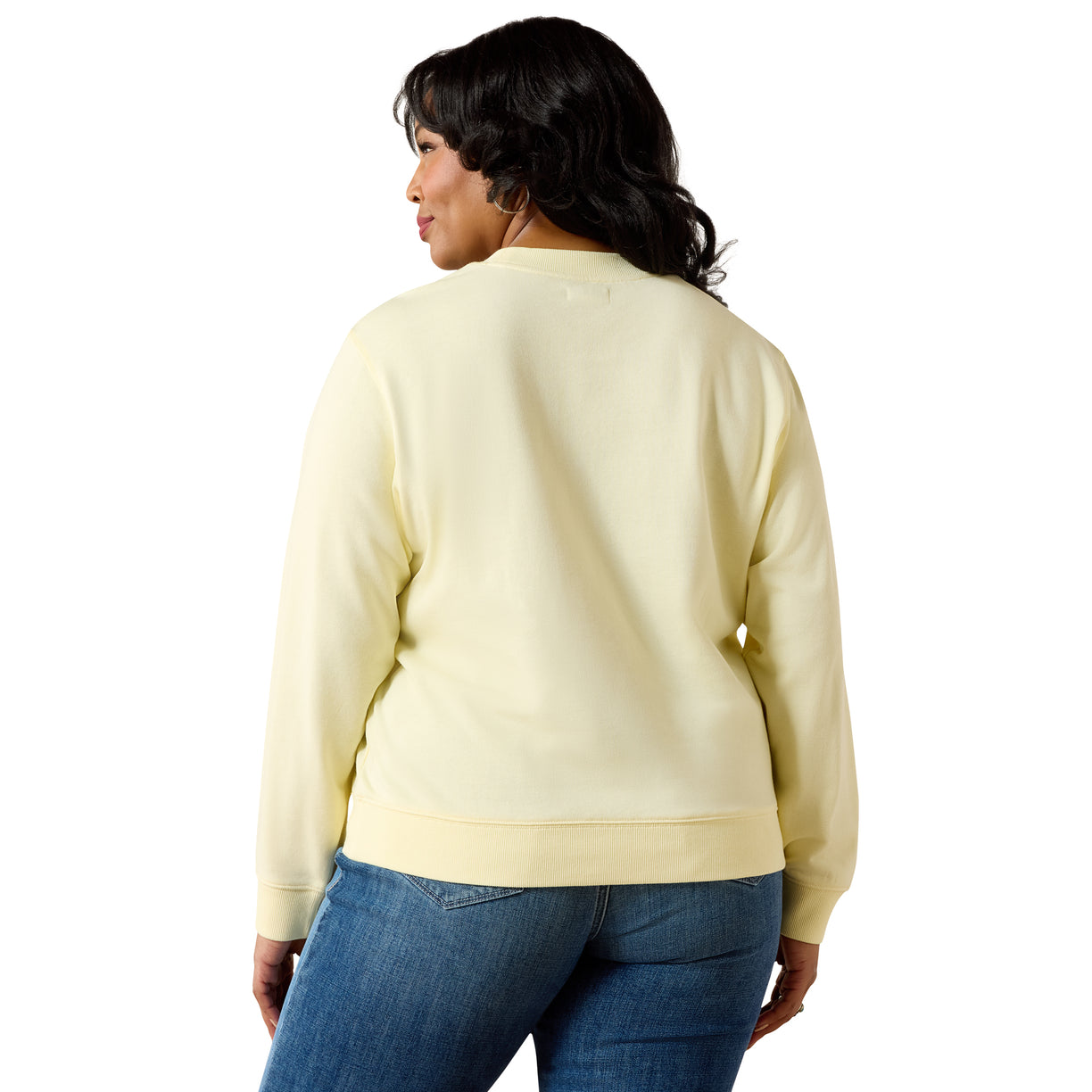 Woman wearing a light yellow sweater and blue jeans on a white background