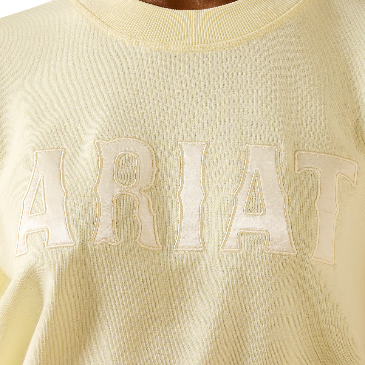 Light yellow sweater with 'ARIAT' branding on a close-up view