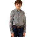 A young boy modeling a long-sleeve button-down shirt with a gray and white geometric pattern, featuring an Ariat logo on the left chest and a red graphic on the right sleeve, paired with dark blue jeans and a brown belt.