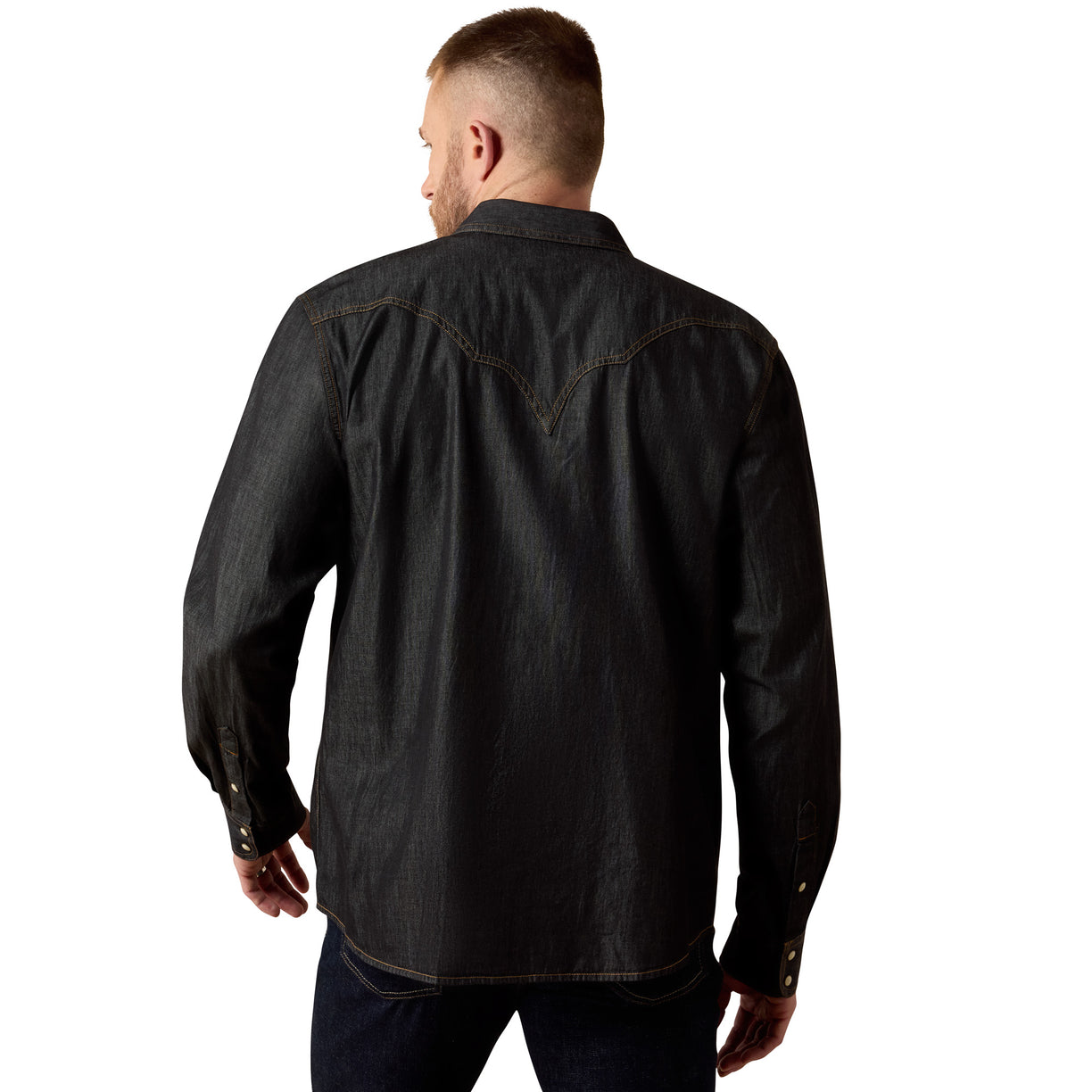 A man viewed from the back wearing a dark charcoal denim western-style shirt with contrast stitching, paired with dark jeans, against a plain white background.