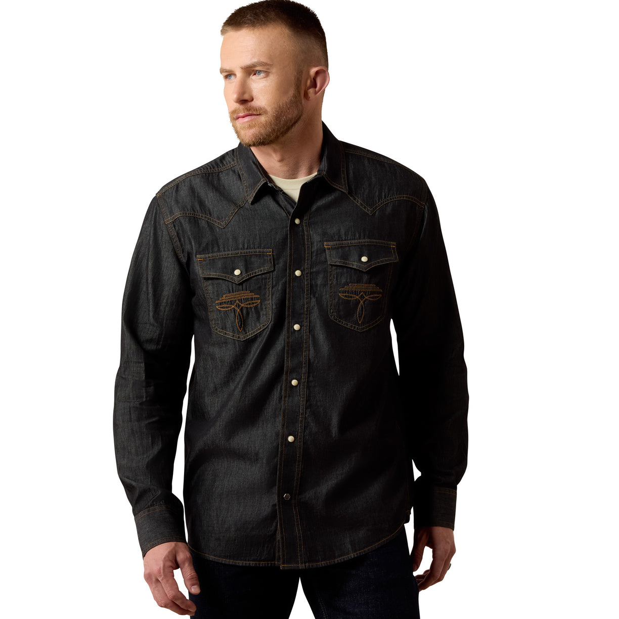 A man wearing a dark washed denim western-style button-up shirt with two chest pockets and embroidered logos on the pockets, photographed against a plain white background.