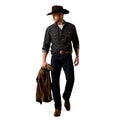 A man wearing a dark gray denim western shirt, dark blue jeans, a brown cowboy hat, and brown boots, holding a brown jacket in one hand against a plain white background.