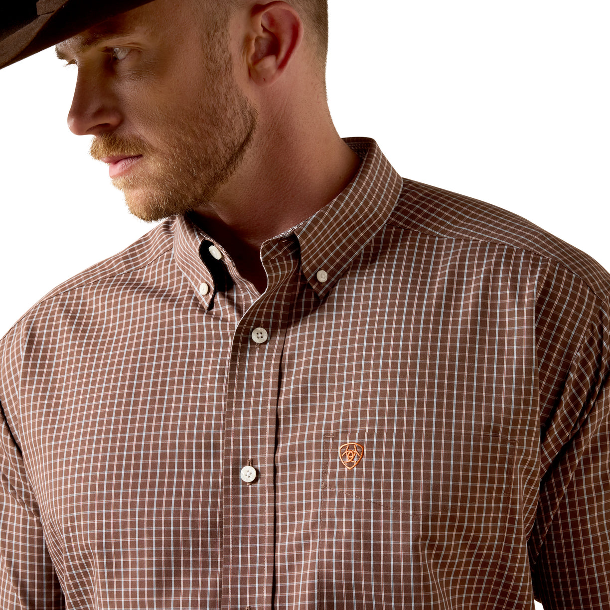 A man wearing a brown and white checkered button-down shirt with a small embroidered logo on the chest, paired with a black cowboy hat against a white background.