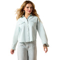 Woman wearing a light blue denim shirt and white pants on a white background
