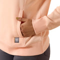 Close-up of a person wearing a light pink hoodie with a brand logo on the chest pocket.