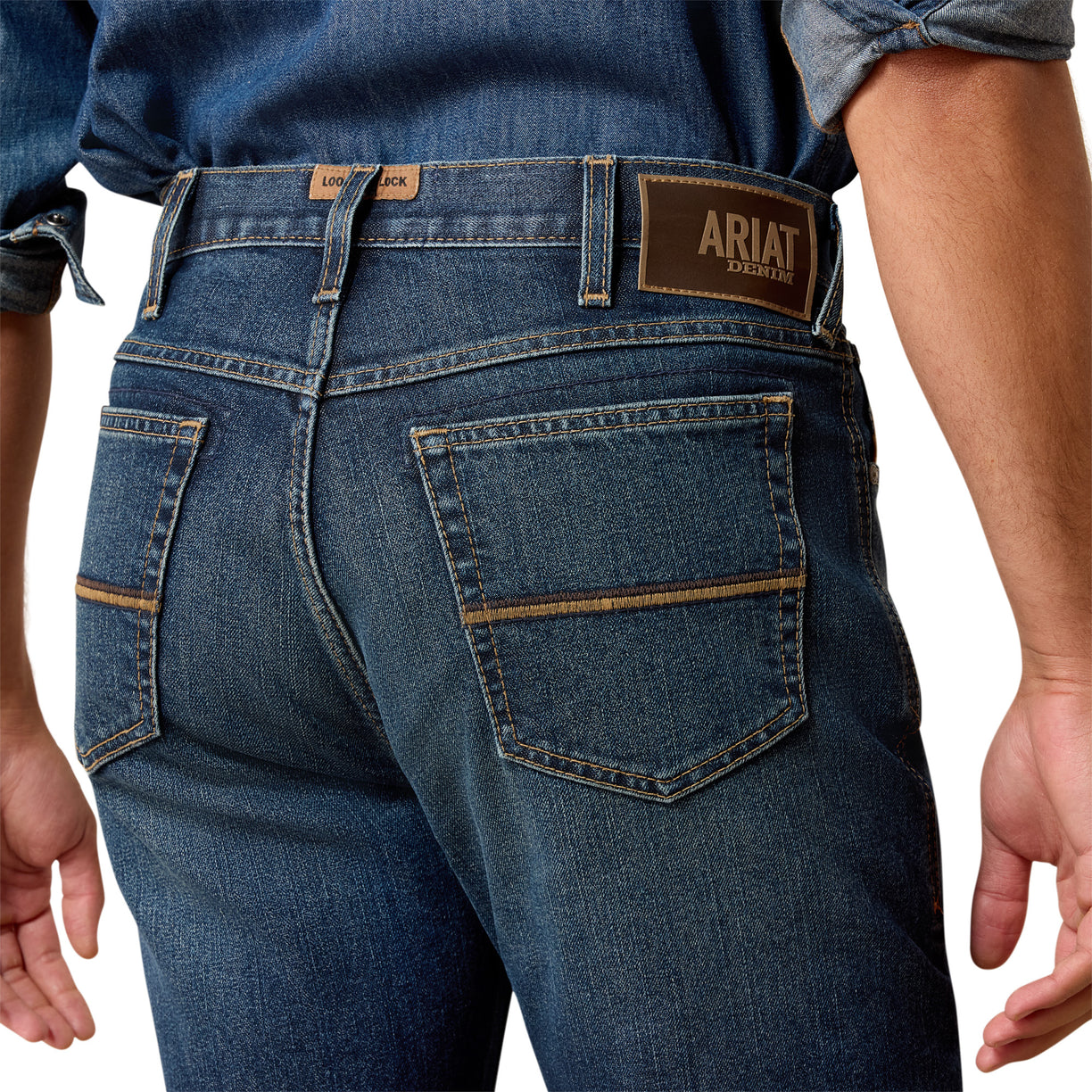 Person wearing blue jeans with Ariat branding on a white background