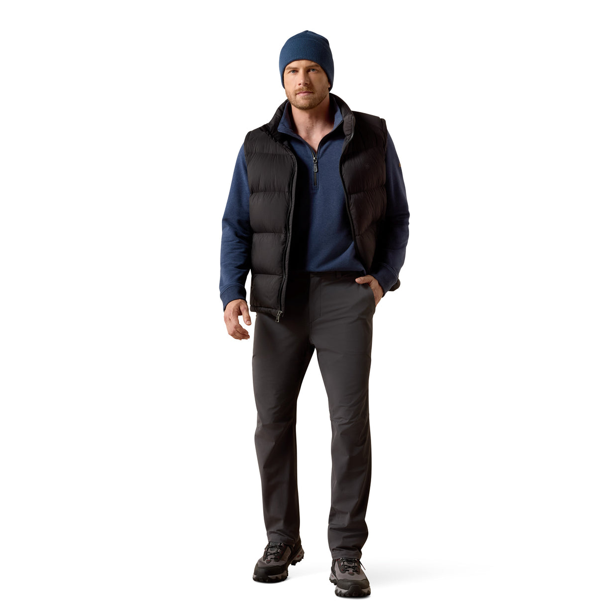Man wearing a blue beanie, black vest, blue shirt, gray pants, and black shoes on a white background