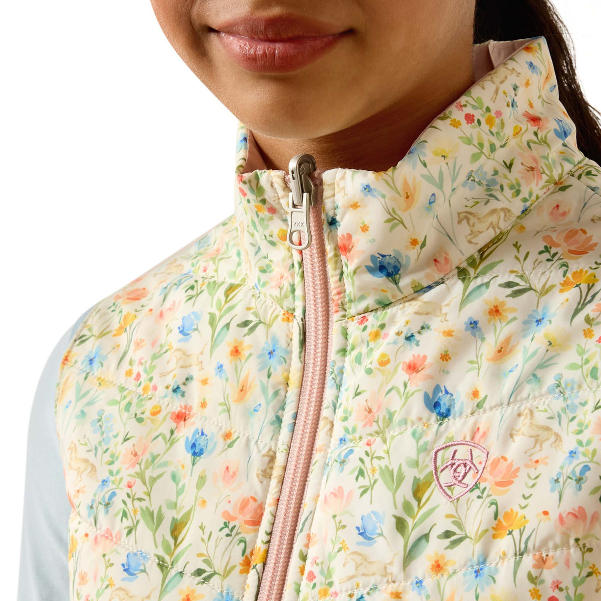 Floral-patterned puffer vest worn by a person, with a focus on the zipper and brand logo.