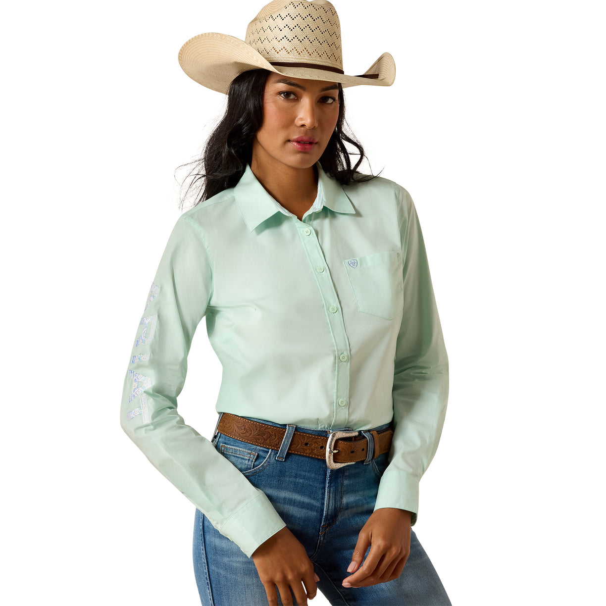A woman modeling a light mint green long-sleeve western shirt with embroidered details on the sleeves, paired with a straw cowboy hat, brown belt, and blue jeans against a white background.