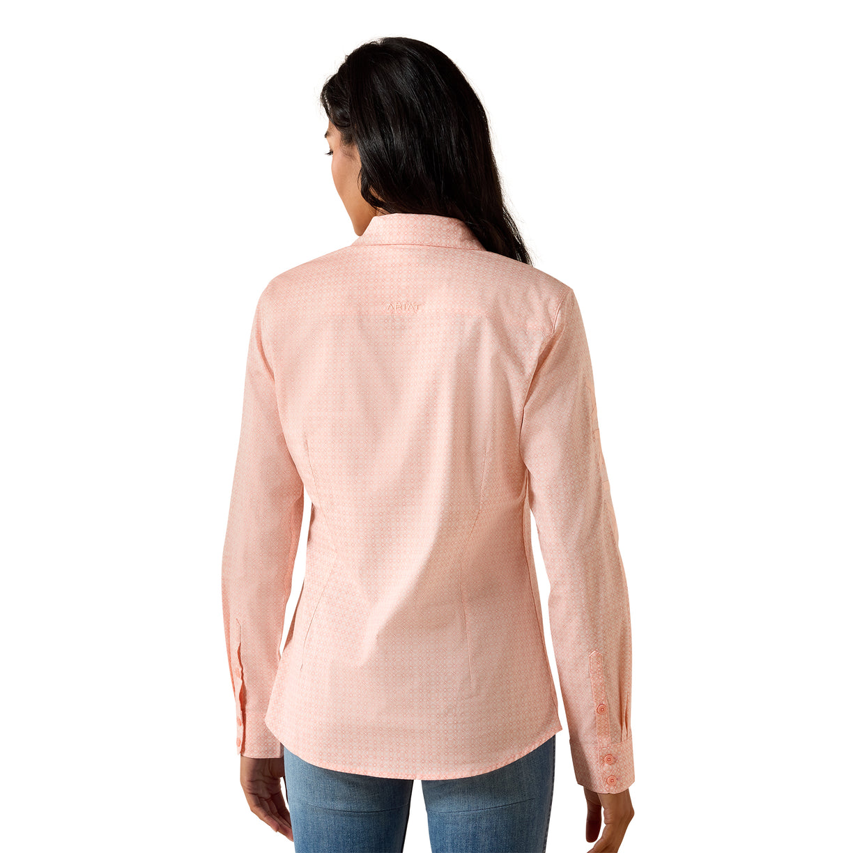 A woman viewed from the back wearing a light peach-pink long-sleeve button-up shirt and blue jeans against a plain white background.