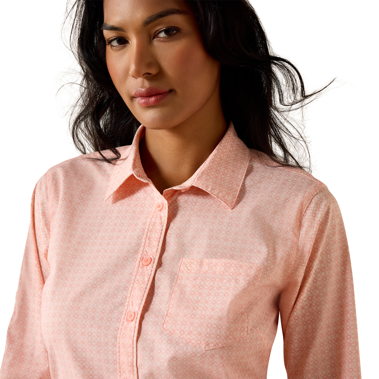 A woman wearing a light pink long-sleeve button-up shirt with a subtle geometric pattern, photographed against a clean white background.