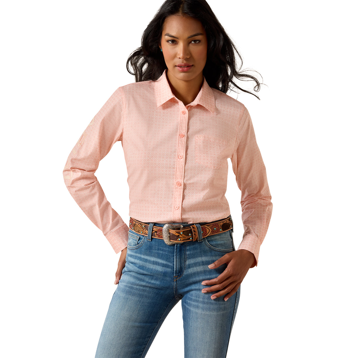 A woman modeling a light pink long-sleeve western-style button-up shirt with a subtle grid pattern, tucked into blue jeans with a brown patterned belt, against a solid white background.