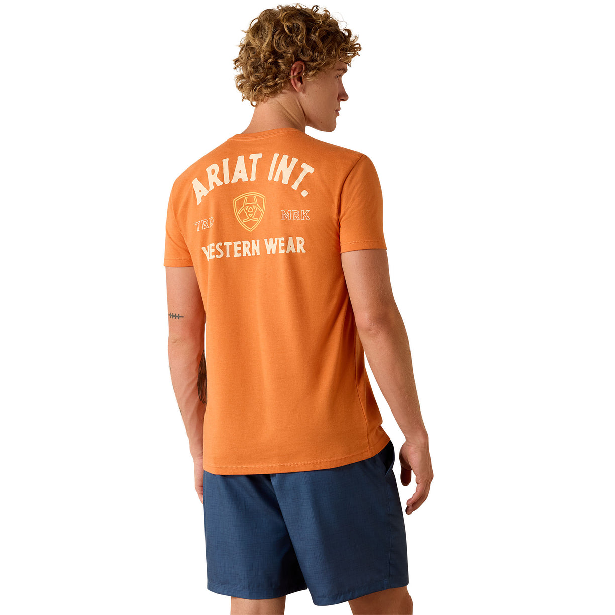 Person wearing an orange t-shirt with 'Ariat Int.' branding on the back, standing against a white background.