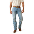 Man wearing light blue Ariat jeans and a beige shirt on a white background