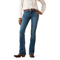 A model wearing a pair of blue western-style boot cut jeans with a brown leather belt, paired with a cream button-down shirt and brown cowboy boots, shown from the waist down on a white background.