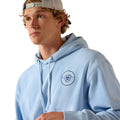 Man wearing a light blue hoodie with a logo on a white background