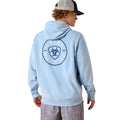 Person wearing a light blue hoodie with a logo on the back, standing against a white background