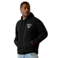 A man wearing a black pullover hoodie with a white embroidered 'Ariat' logo on the left chest, paired with light blue jeans, set against a plain white background.