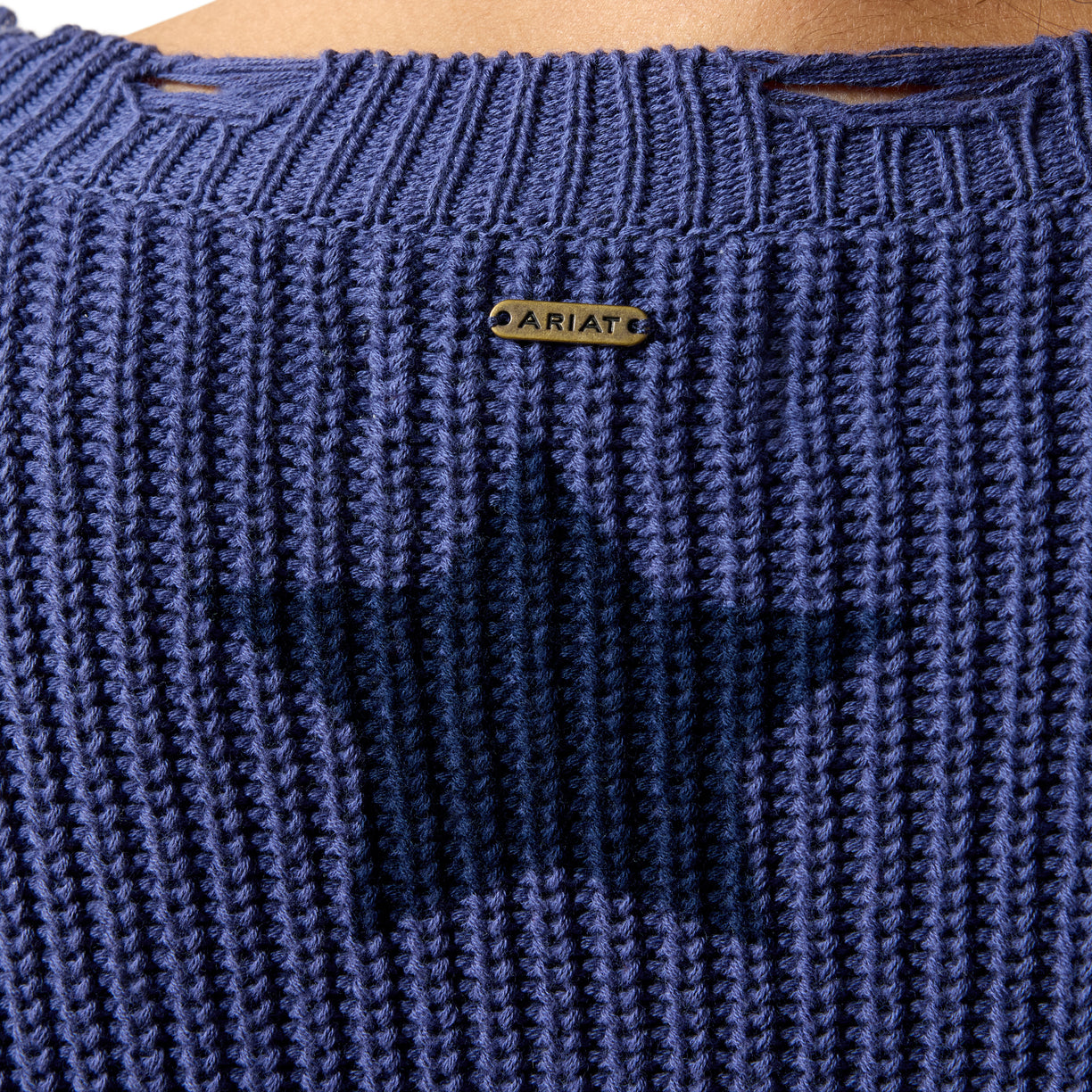 Close-up of a blue knitted garment with 'Ariat' branding on a wooden surface.