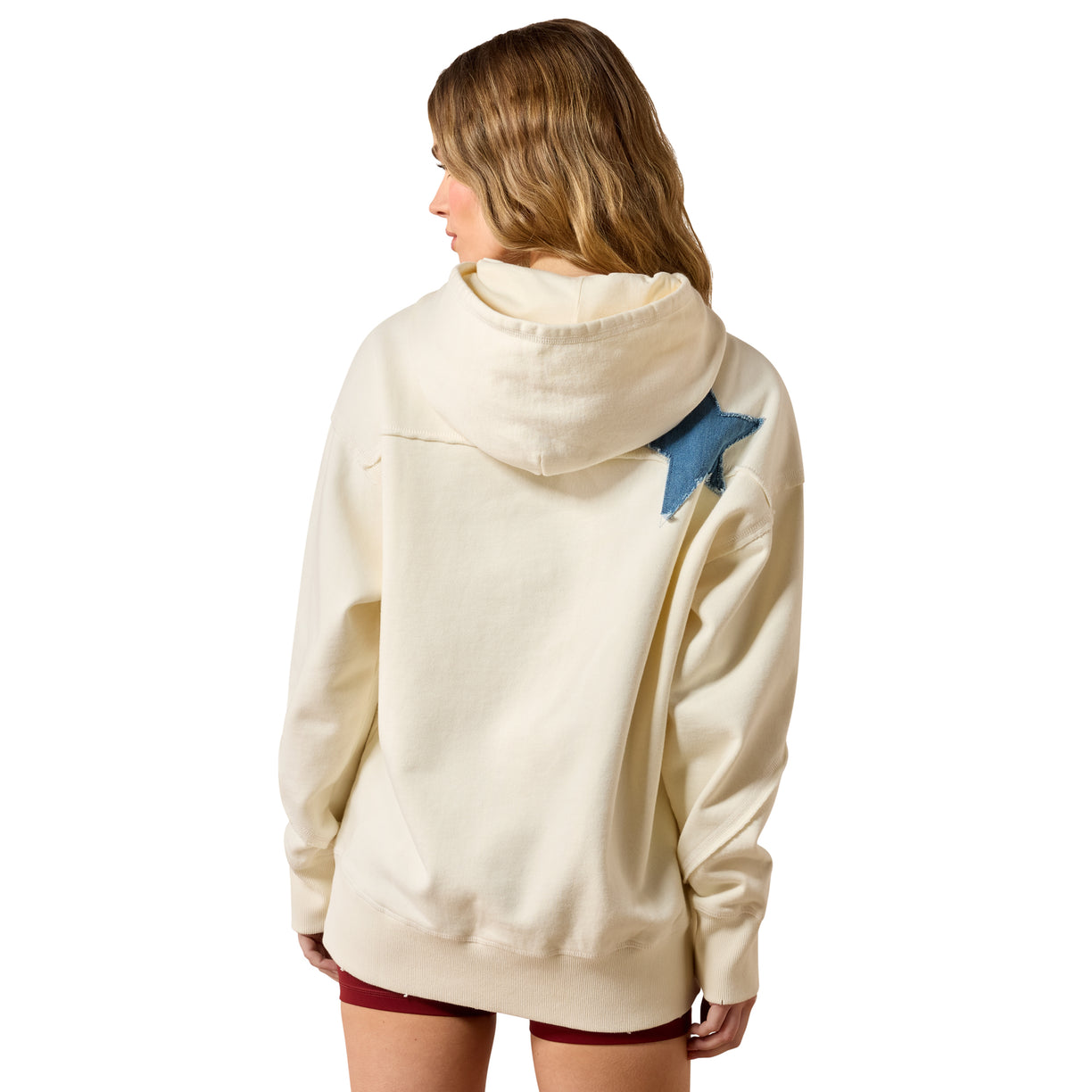 Person wearing a cream-colored hoodie with a blue patch on the back, standing against a white background