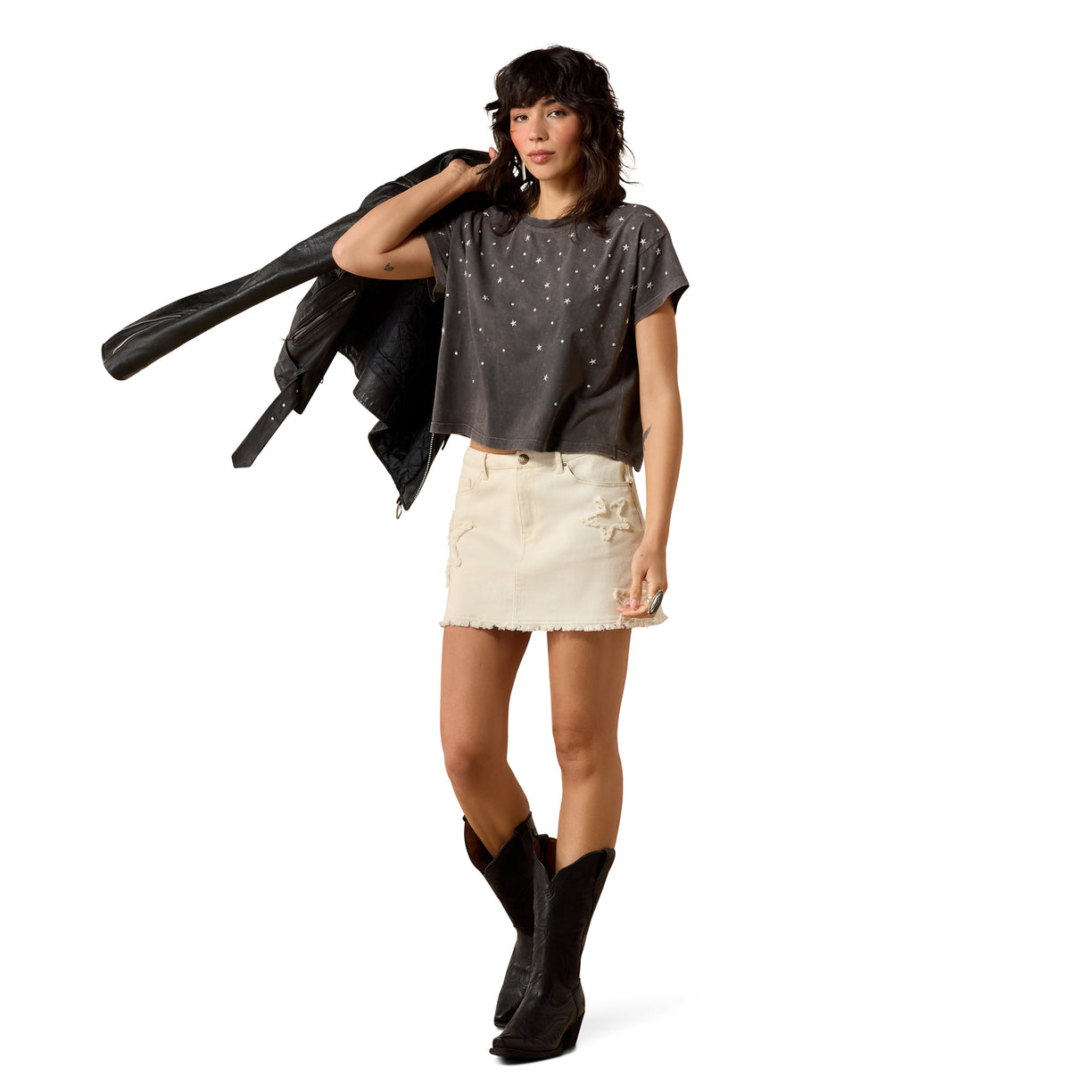 Woman wearing a dark gray t-shirt with star patterns, white shorts, and black boots on a white background