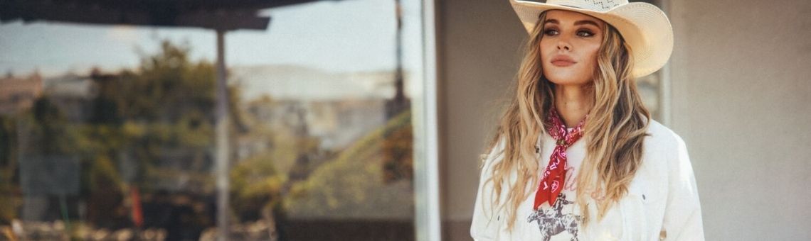 A promotional banner for the 'Western Serenade Fashion Collection' featuring a model wearing a white cowboy hat, a white shirt, and a red bandana, set against an outdoor background.