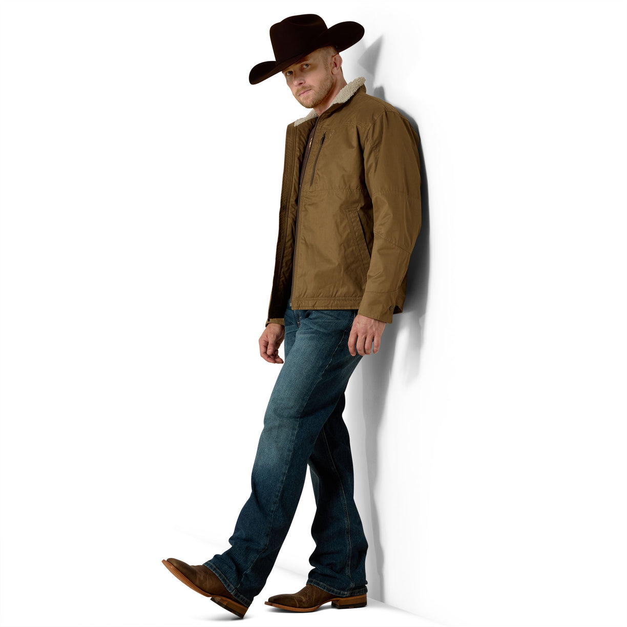 Man wearing a brown jacket, blue jeans, and a cowboy hat against a white background