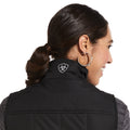 Woman wearing a black vest with a logo on the back against a white background