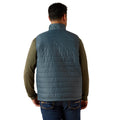 Person wearing a blue puffer vest over a green long-sleeve shirt on a white background