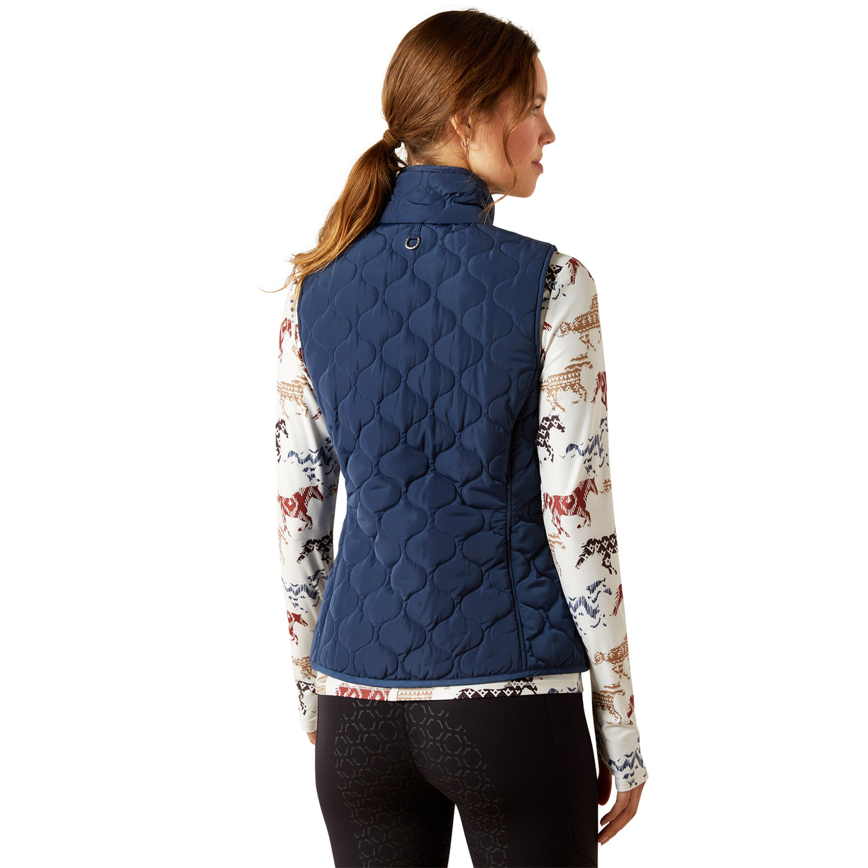 Woman wearing a blue quilted vest over a patterned shirt on a white background