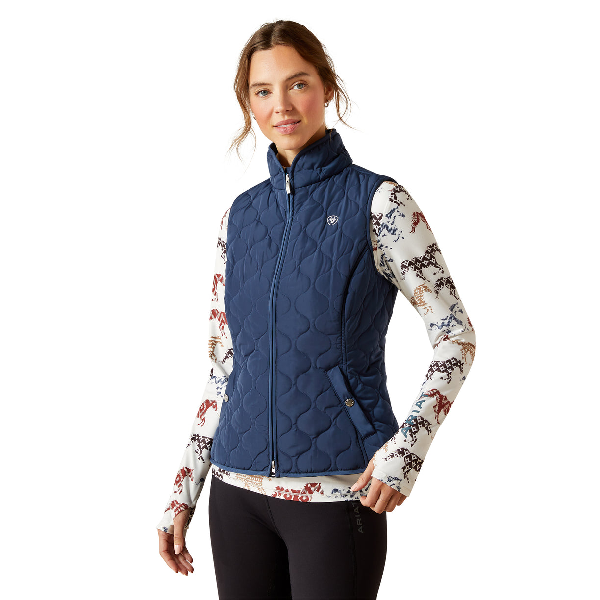 Woman wearing a blue quilted vest over a patterned shirt on a white background
