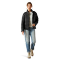 Woman wearing a black puffer jacket, gray shirt, blue jeans, and beige boots on a white background