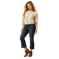 Woman wearing a beige sweater with 'Chase' branding, blue jeans, and brown boots on a white background.