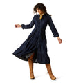 Woman wearing a navy blue dress with long sleeves and a belt, standing on a white background.