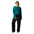 Woman wearing teal long-sleeve top and dark patterned pants on a white background