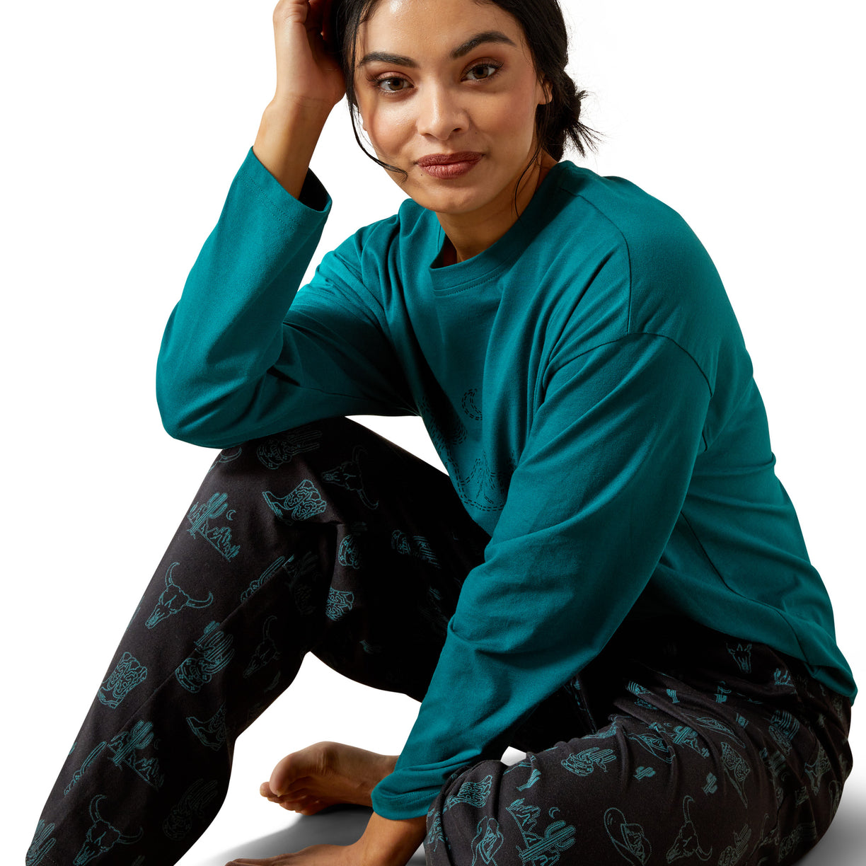 Woman wearing a teal long-sleeve top and dark patterned pants on a white background