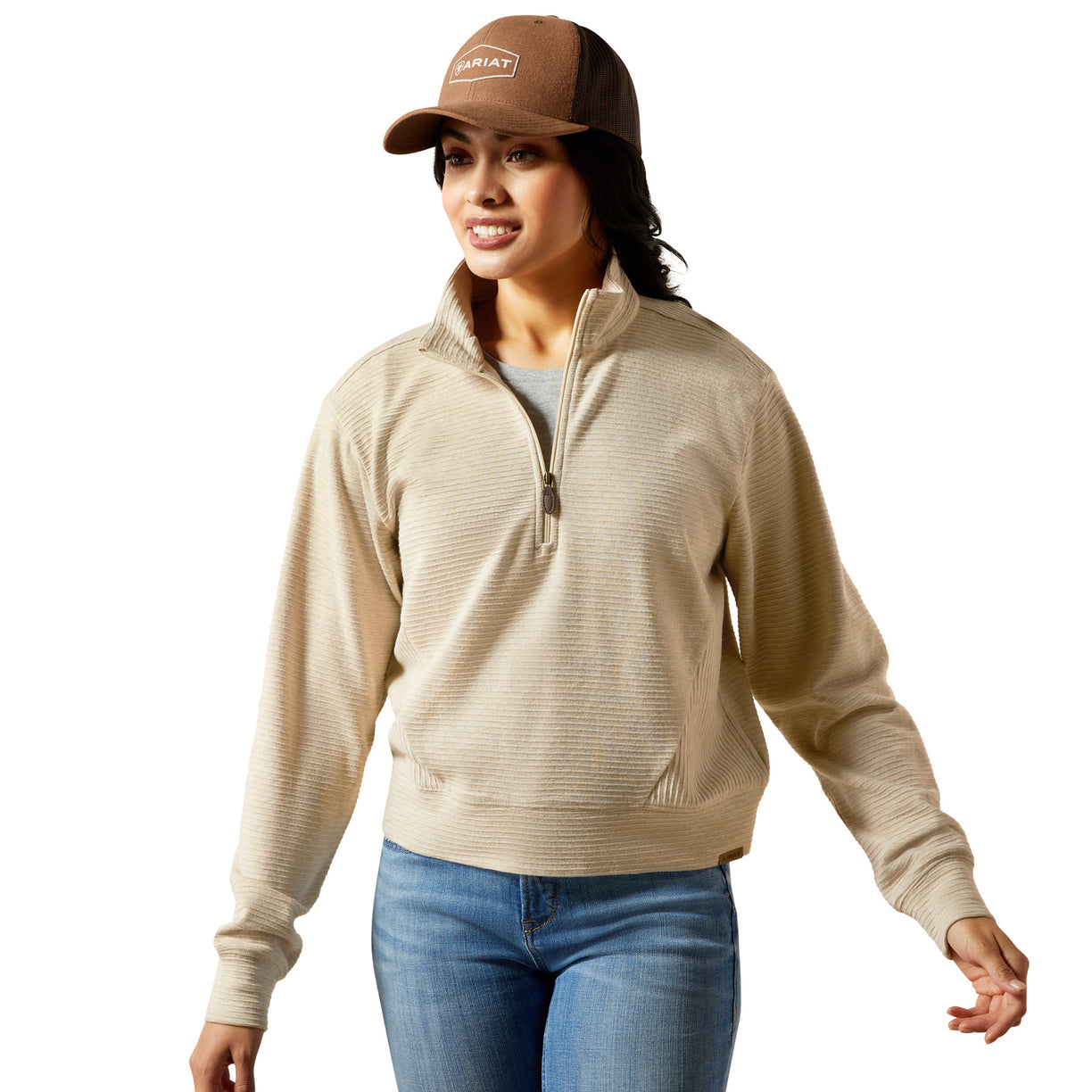 Woman wearing a beige sweater, brown cap, and blue jeans on a white background