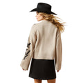 Woman wearing a beige sweater with black feather designs and a black skirt on a white background