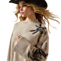 Woman wearing a beige sweater with black floral embroidery on a white background